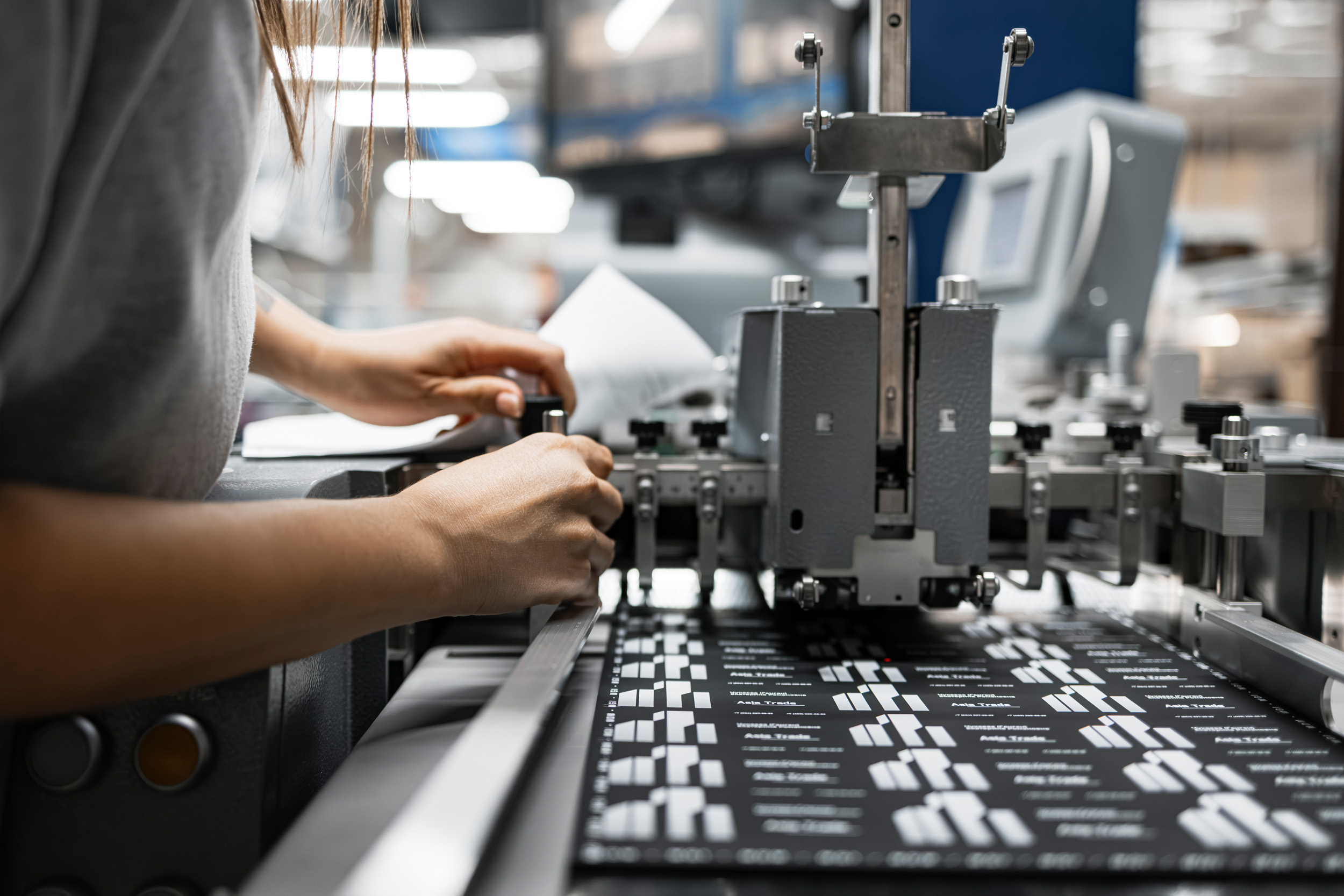 Woman operating a precision cutting machine in a factory setting, processing printed materials.